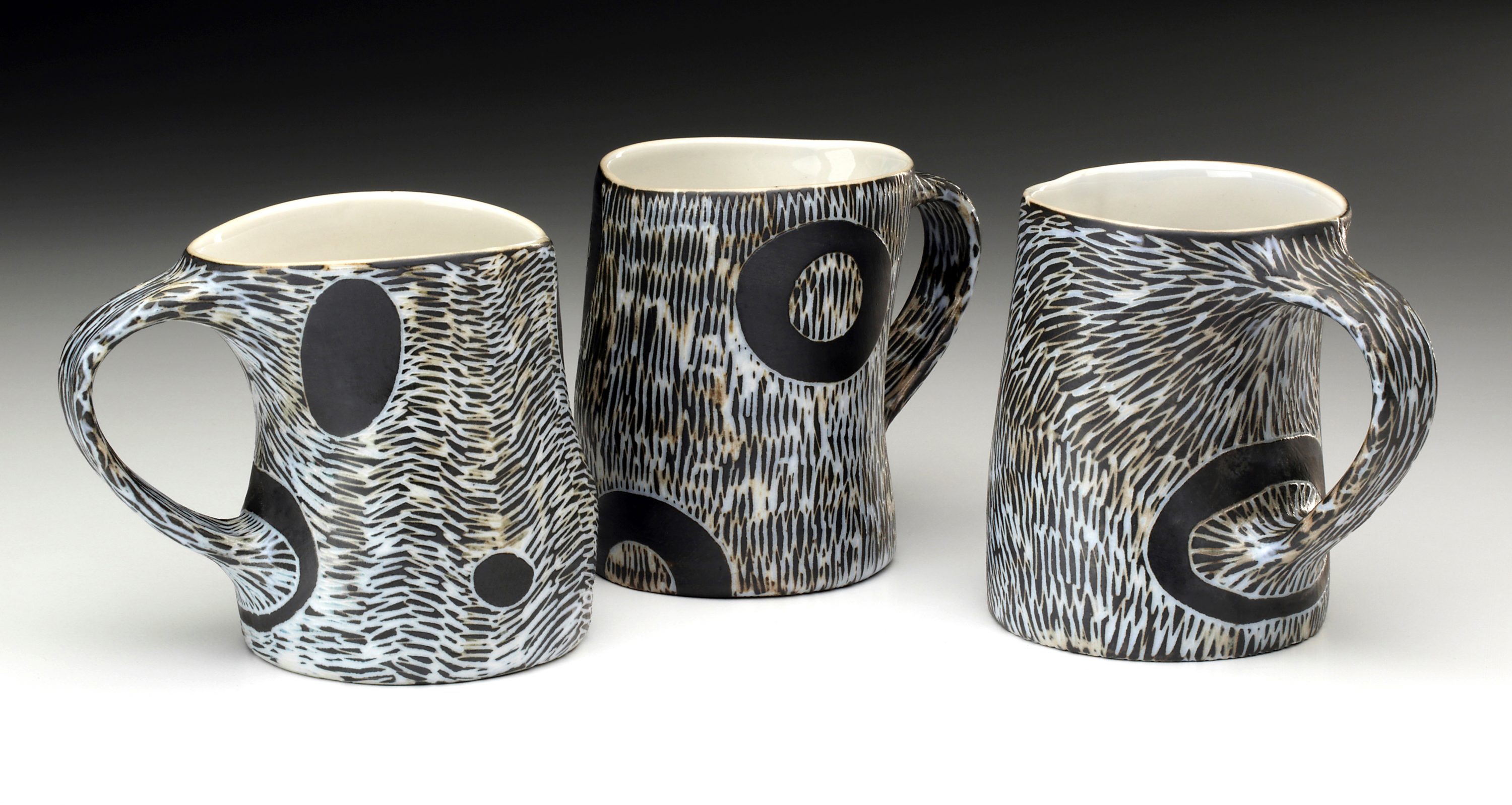 James Guggina writes, "I have been a potter since graduating from Mass Art in 1994. I make pots that are sturdy and user-friendly for everyday use. I like the idea that my work can become a part of your everyday life and that it brings a little bit of beauty into your morning cup of coffee, a sandwich at lunchtime, or a dinner with family and friends." These mugs are his newest work. Coffee mugs; wheel-thrown and altered porcelain. Black and white sgraffito, wood fired with salt glaze. Approx 4.25" tall Florence, MA 01062