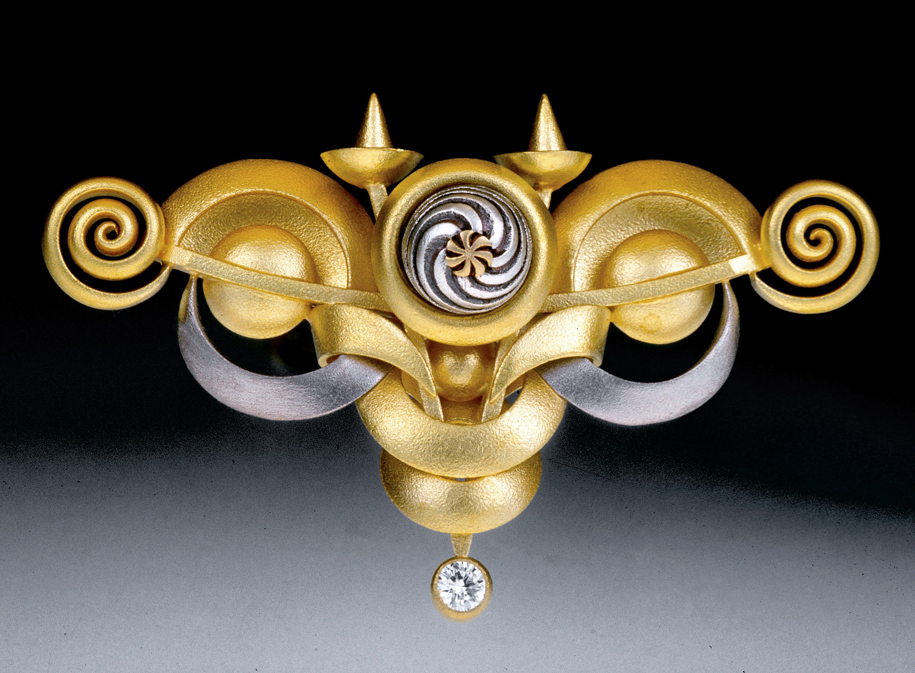 Aaron Macsai actually alloys his own gold, which allows him to create more colors than the standard yellow, white and pink. Intricately carved, Mascai’s ebullient bracelets, brooches, pendants and earrings are recognized for their integrity of design. His work was selected for the prestigious national touring exhibition “The Art of Gold”. "Pinwheel Brooch", 14k gold, inlaid with patterns the artist creates in silver, gold and gemstones. Morton Grove, IL 60053; Jewelry